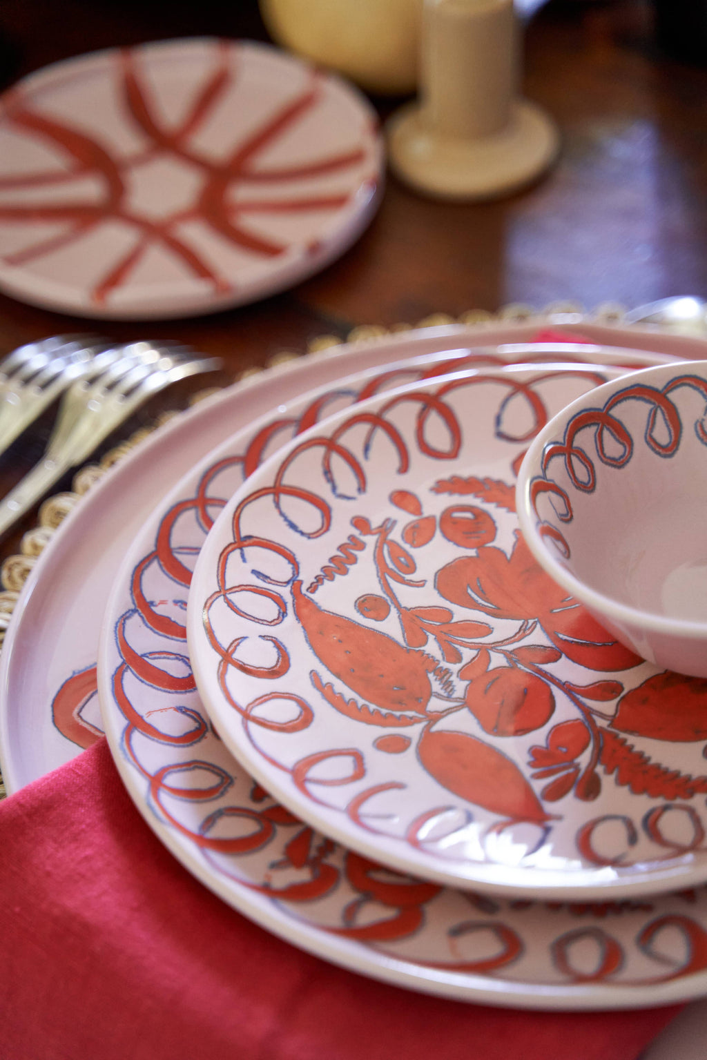 Stack of patterned Amalfi Collection pink ceramic plates on a table with a red napkin.