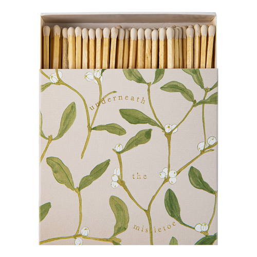 An Archivist square matchbox package of wooden matches with a beige cover printed with green mistletoe branches, white berries, and the words 'underneath the mistletoe.' The matches are arranged upright inside an open box against a plain white background.