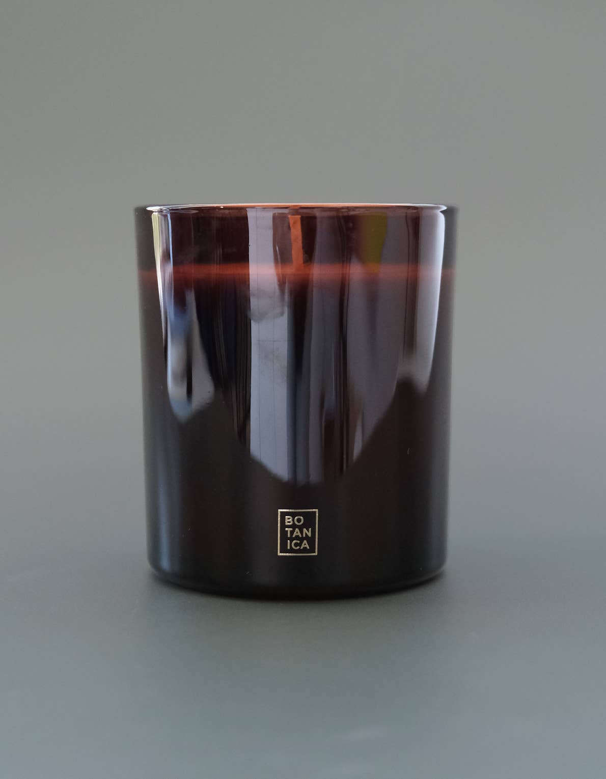 Botanica burgundy mulled cider candle with a brand logo on a gray background