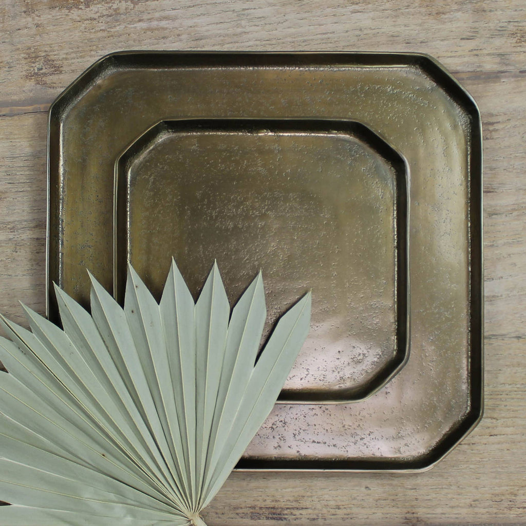 Set of two brass trays on a wooden surface with a leaf.