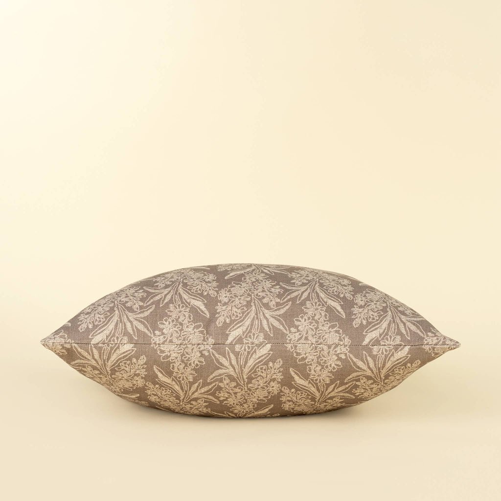 A square pillow with a brown and beige damask floral pattern, photographed against a solid cream background.