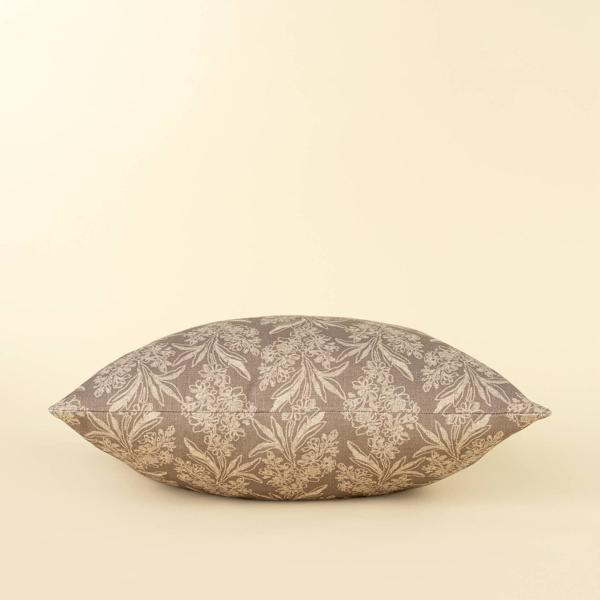 A square pillow with a brown and beige damask floral pattern, photographed against a solid cream background.