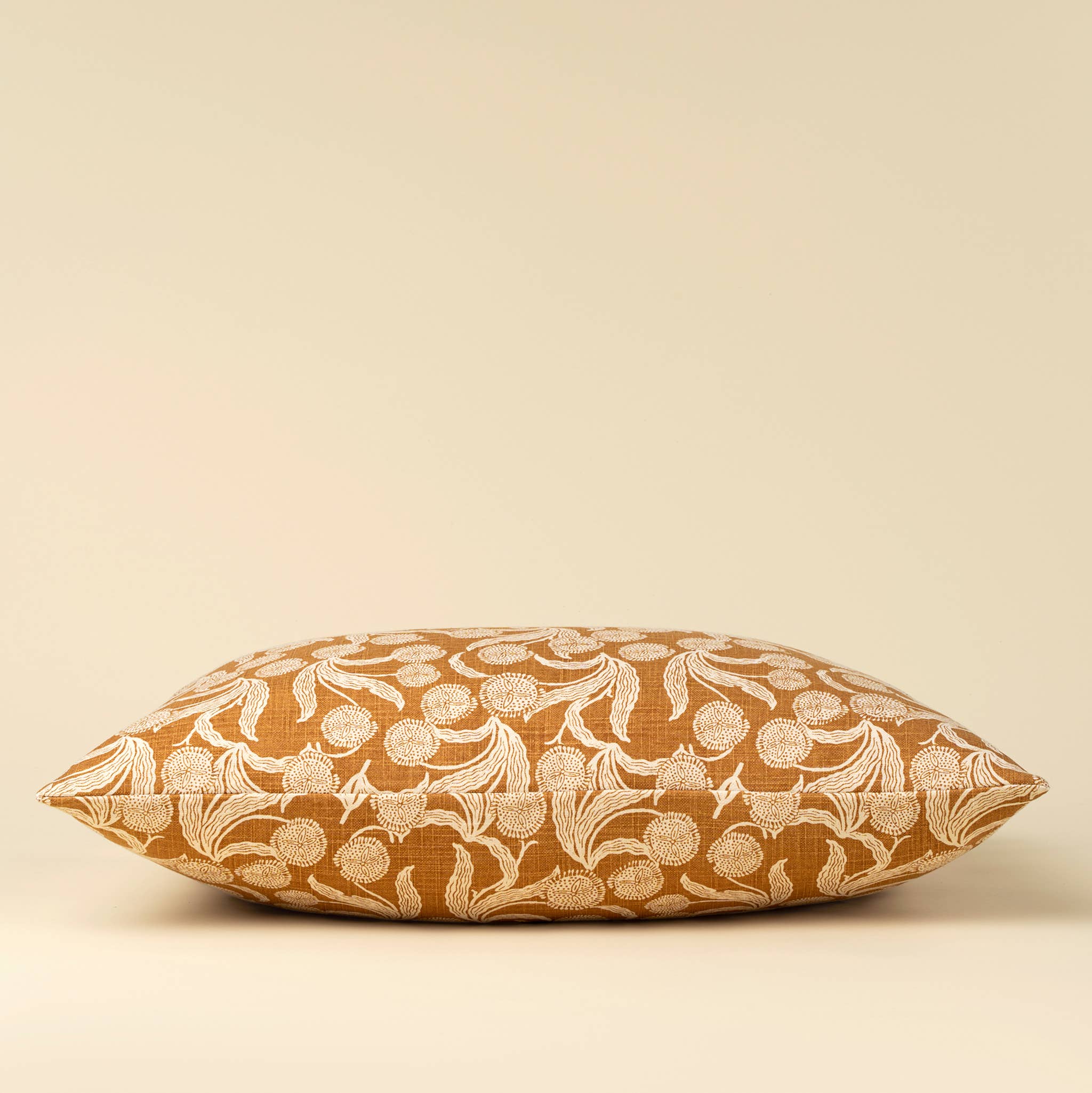 A rectangular decorative throw pillow with a warm mustard-yellow background and an intricate cream floral and vine pattern, shown against a solid light beige background.