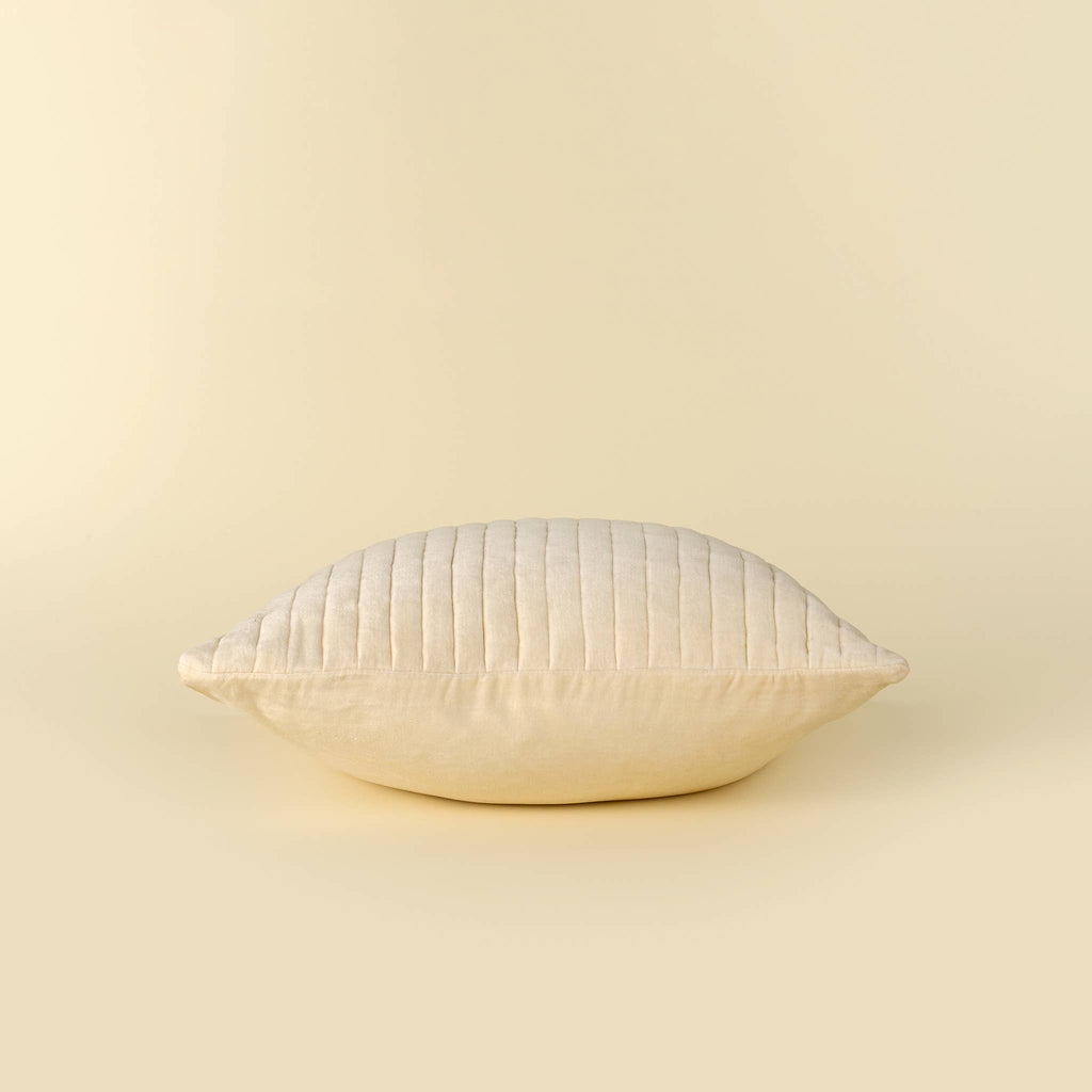 A square cream-colored pillow with vertical channel tufting, shown against a solid cream background.