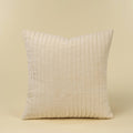 A square throw pillow in an ivory velvet fabric with vertical pleats, shown against a solid beige background.