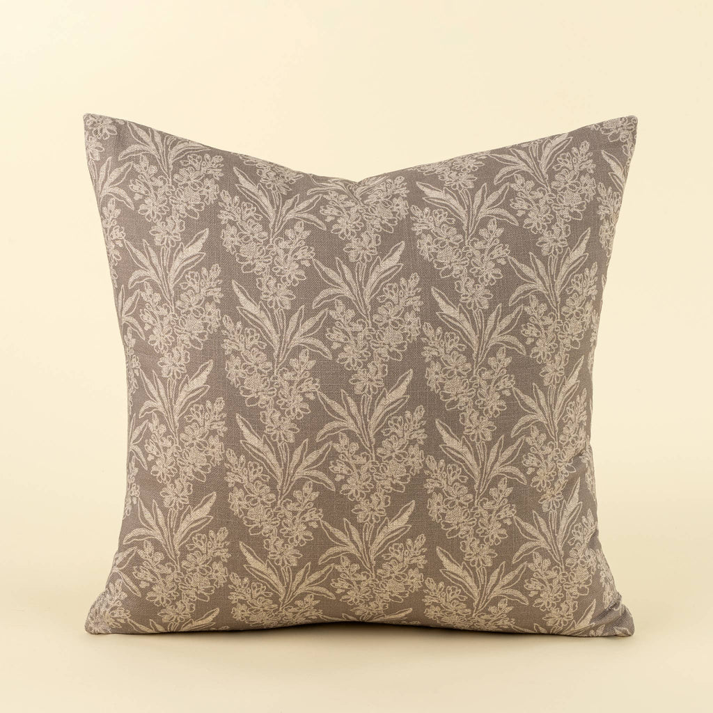 A square throw pillow featuring a classic damask floral pattern in taupe and beige, set against a solid cream background.
