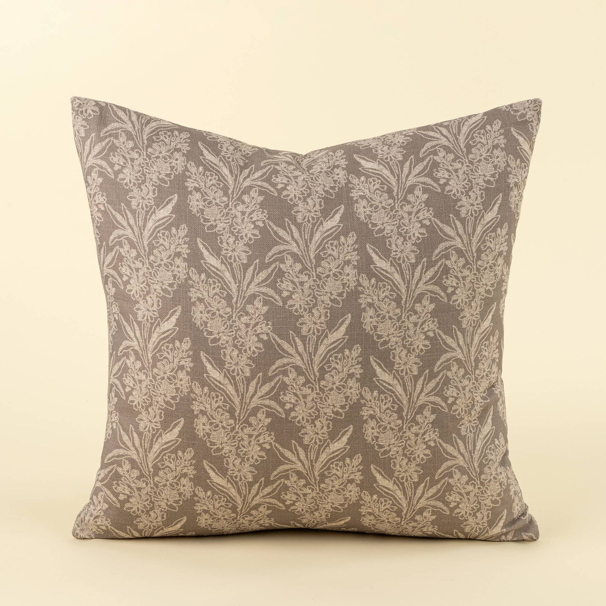 A square throw pillow featuring a classic damask floral pattern in taupe and beige, set against a solid cream background.