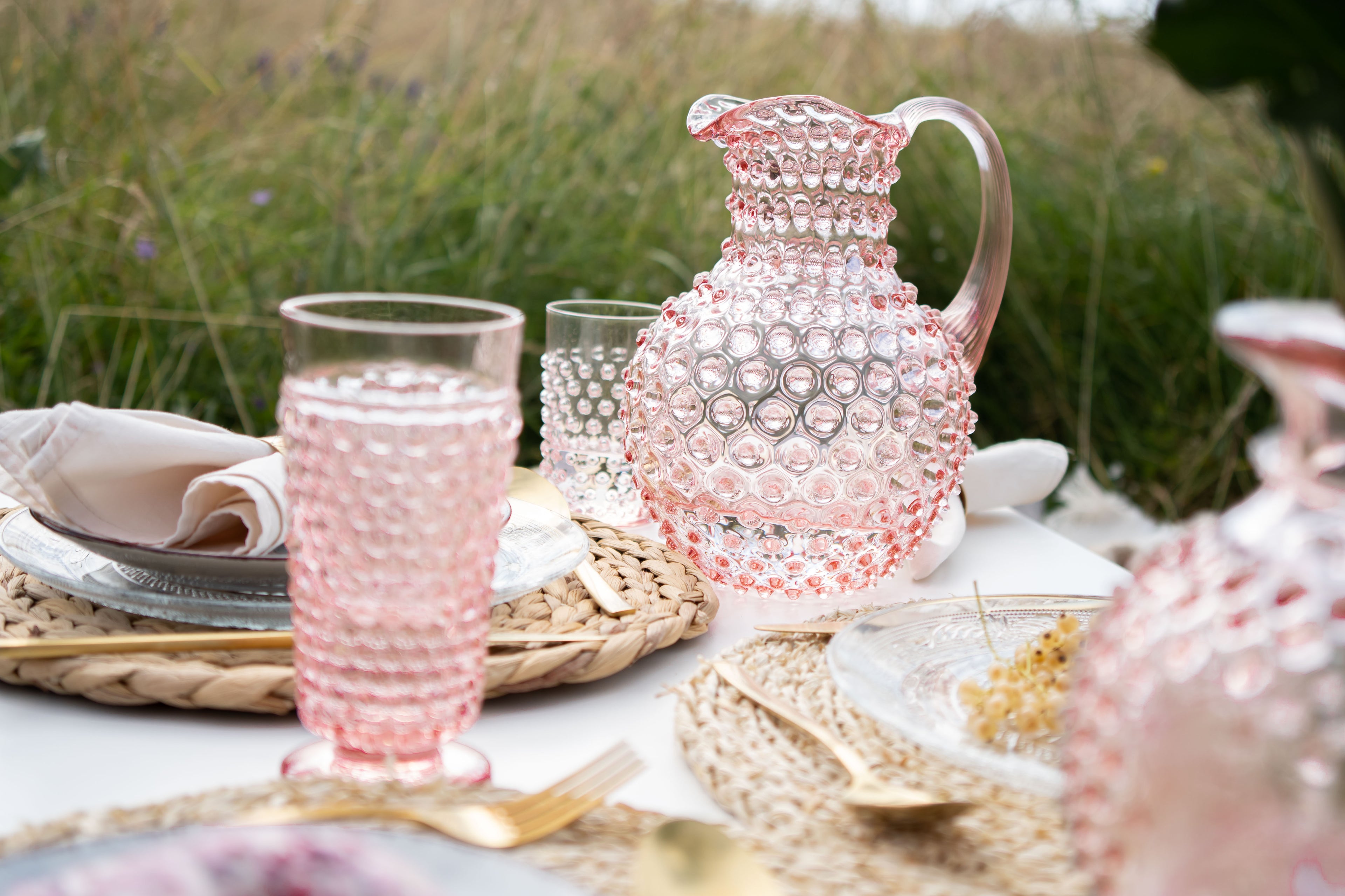 Pink Klimchi hobnail glassware set on a table outdoors with natural background