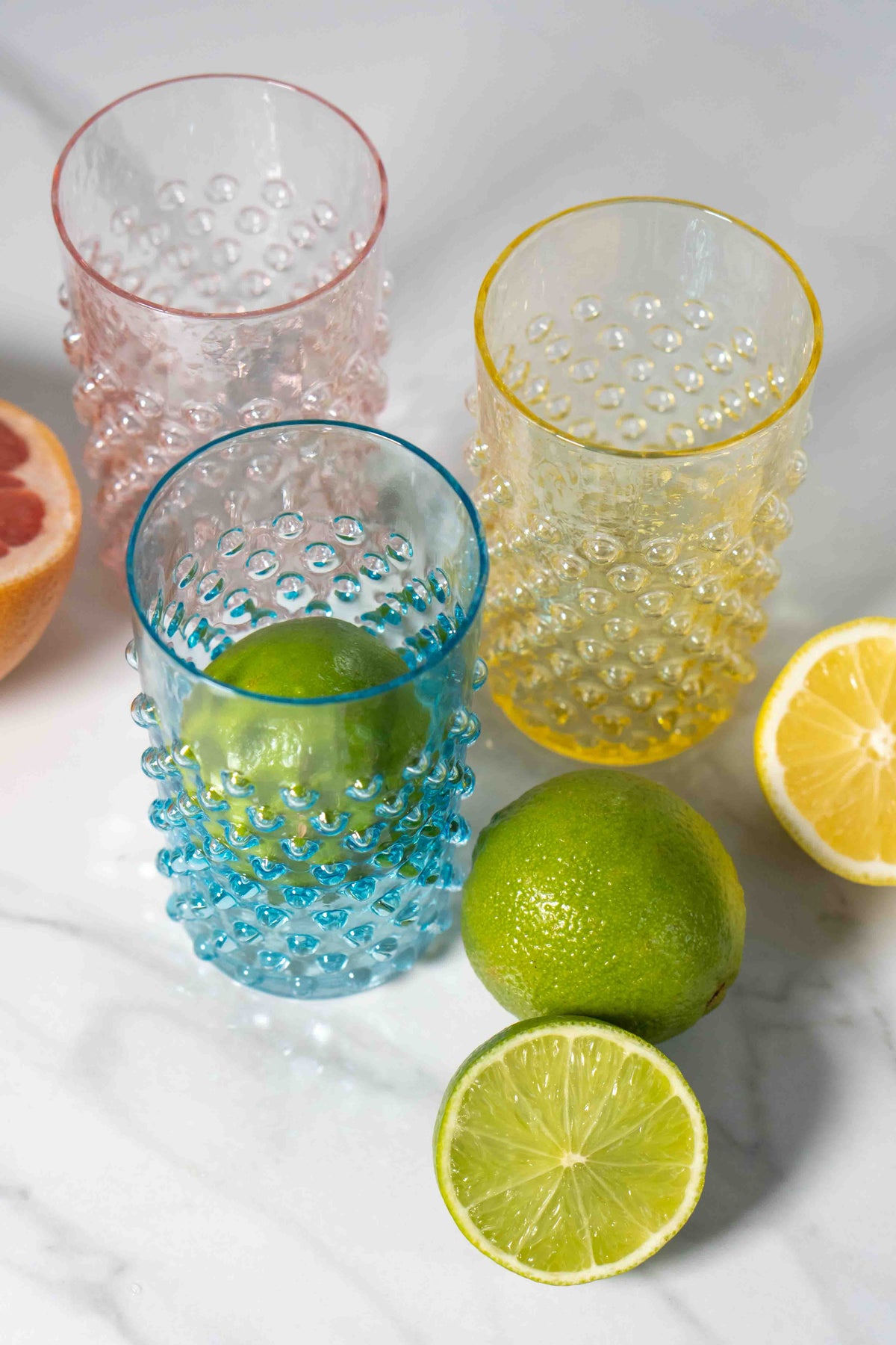 Colorful Klimchi hobnail glass tumblers with citrus fruits on a marble surface