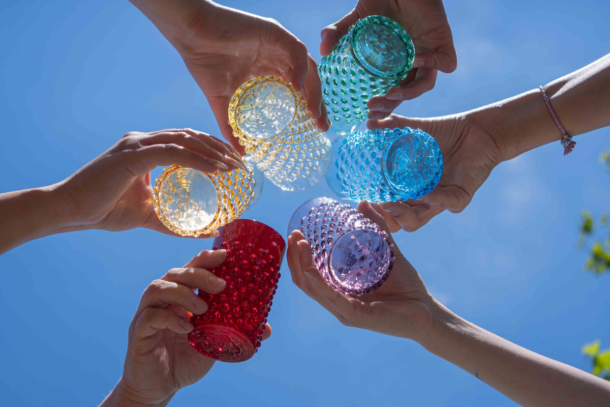 Hands holding colorful Klimchi hobnail tumblers against a blue sky