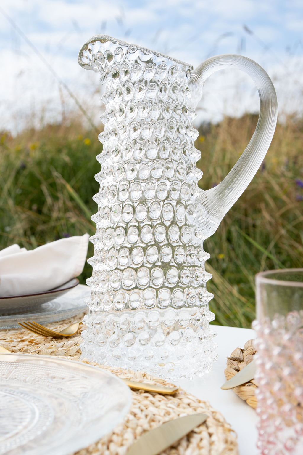 Clear Klimchi hobnail tall glass pitcher on a table with a natural background