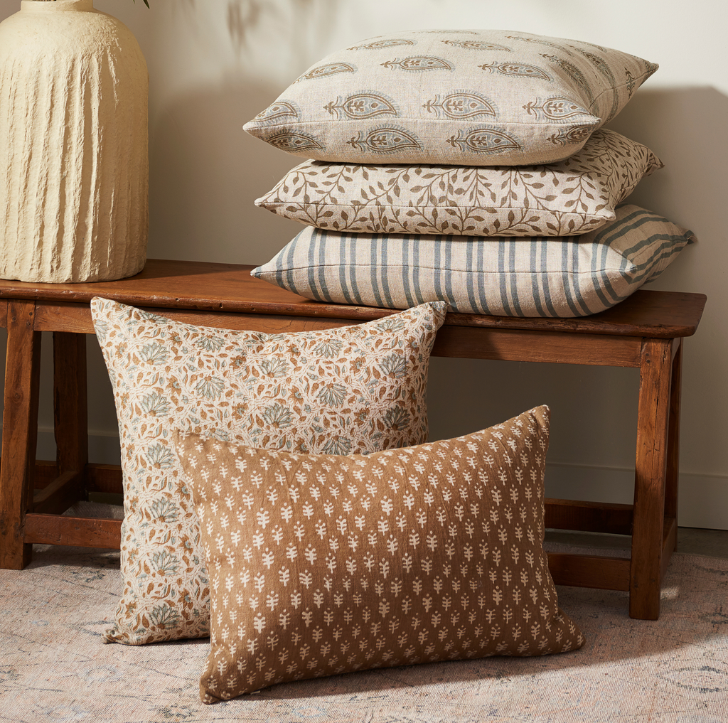Patterned Liam and Lana linen pillows with down fill on a wooden bench against a neutral wall.