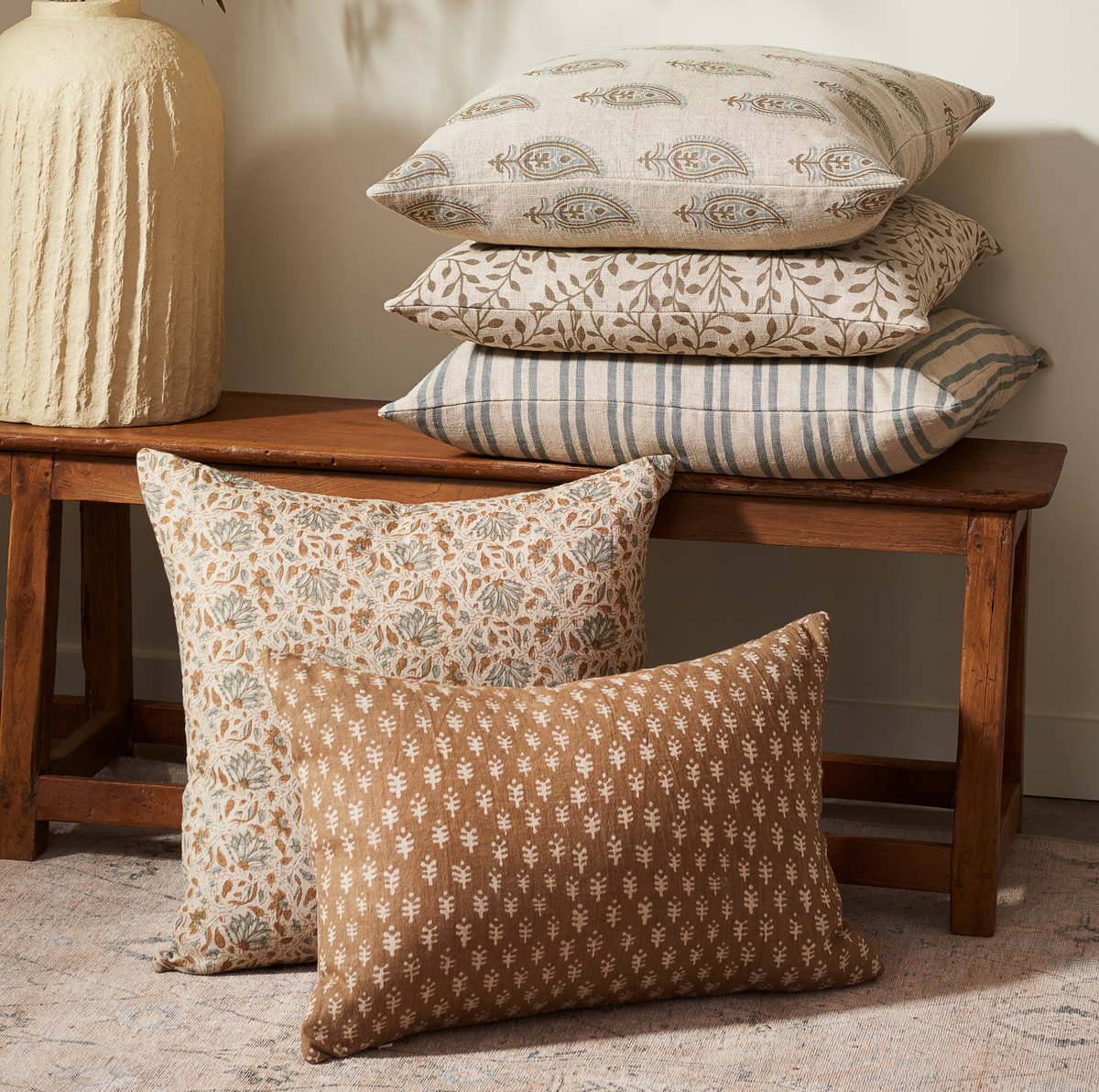 Patterned Liam and Lana linen pillows with down fill on a wooden bench against a neutral wall.