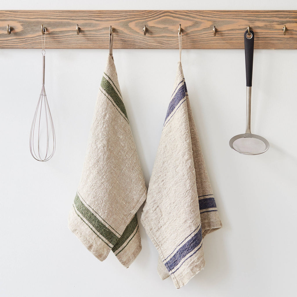 Two Linen Hand Towels hanging from a wooden rack. One with blue stripes on a natural linen background, the other with green stripes on a natural linen background.