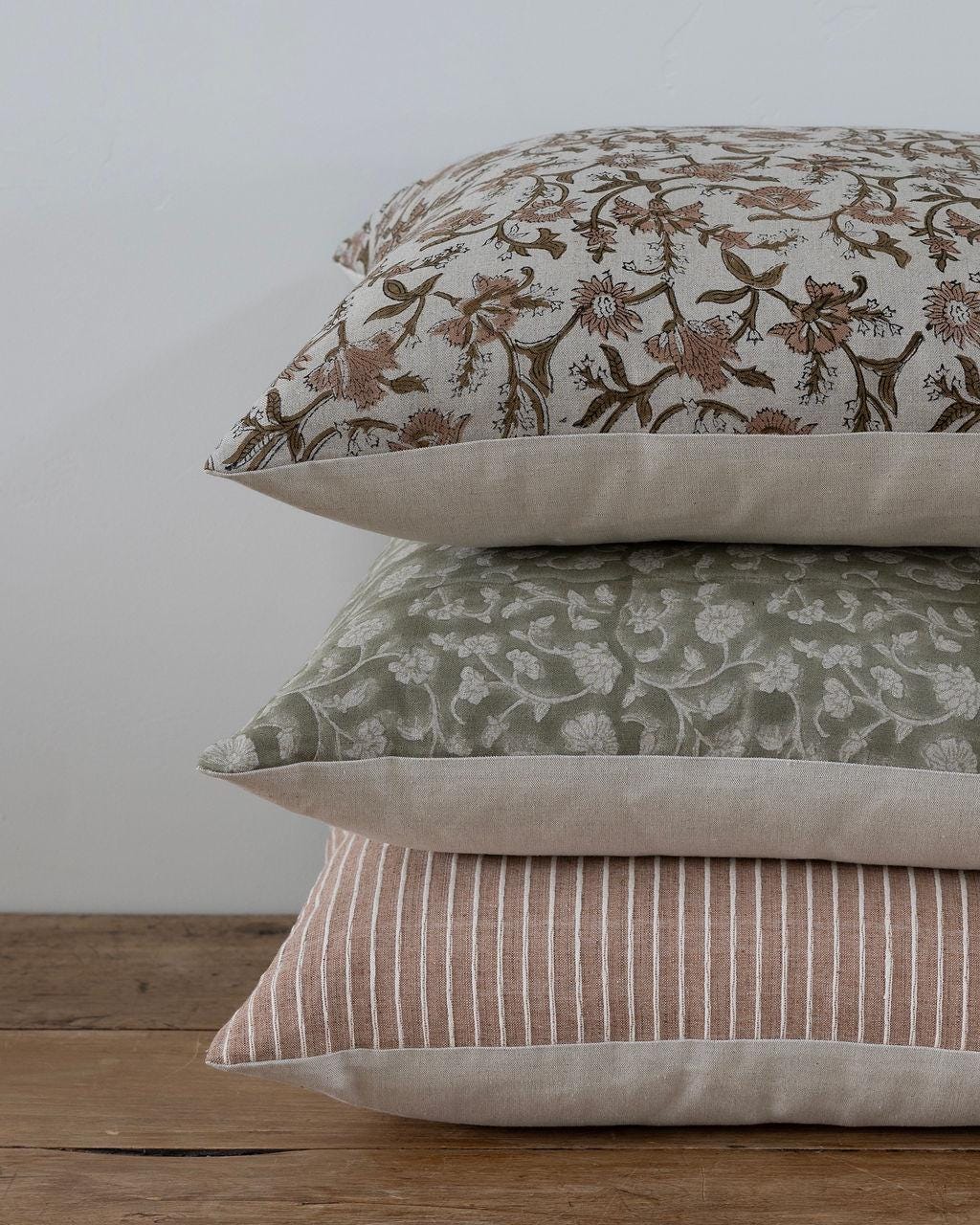 Stack of three patterned Linen & Cloth pillows on a wooden surface with a white background