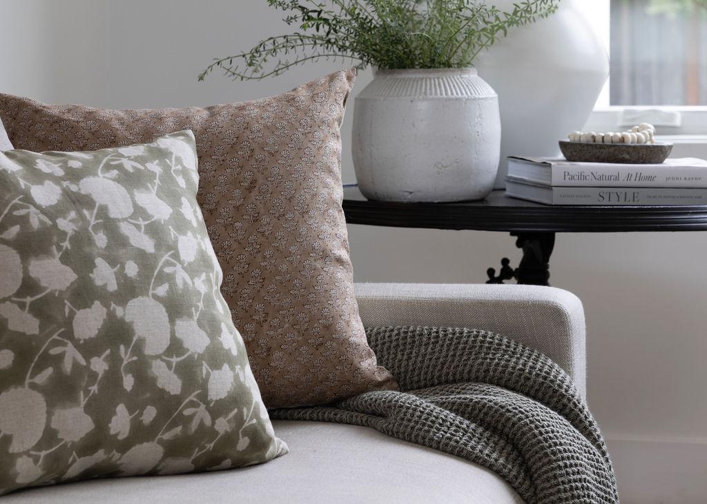 Linen & Cloth patterned throw pillows and a blanket on a sofa with a small table in the background