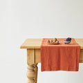 Wooden table with a baked clay linen runner and small bowls of fruit on a light background