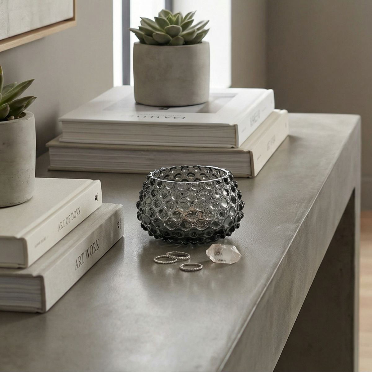 Decorative setup with books, a glass bowl, and succulents on a concrete surface with a small hobnail bowl