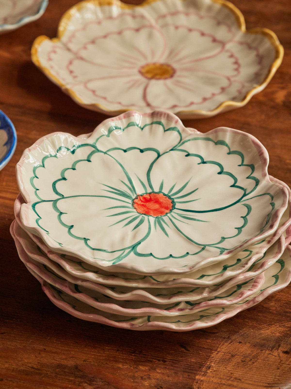 Stack of colorful decorative handmade ceramic plates in a floral shape on a wooden surface