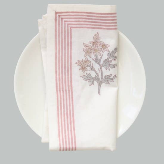 Cotton Napkin with pink and green floral block print design and pink stripes on a white plate against a gray background