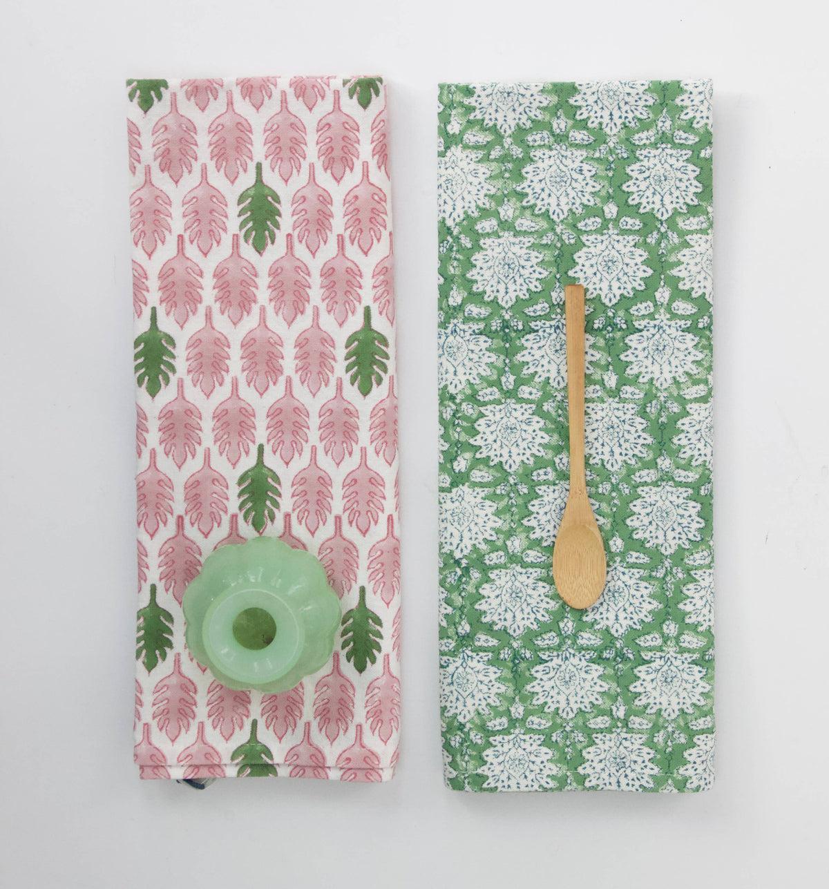 Two block print patterned dish towels or tea towels with a wooden spoon on a white background