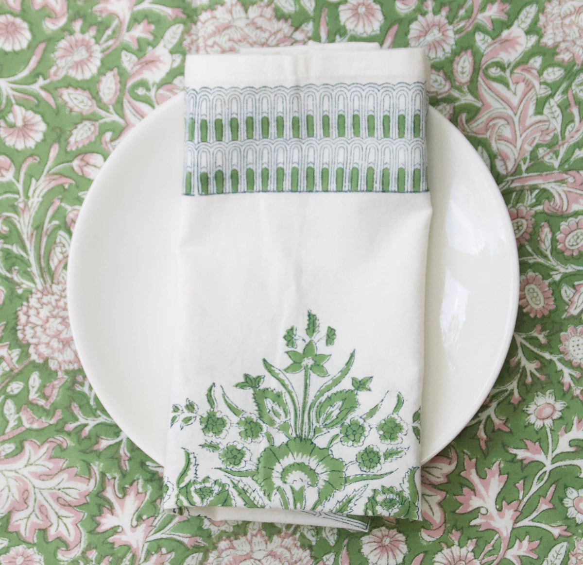 White plate with a green and white block print napkin on a floral tablecloth.