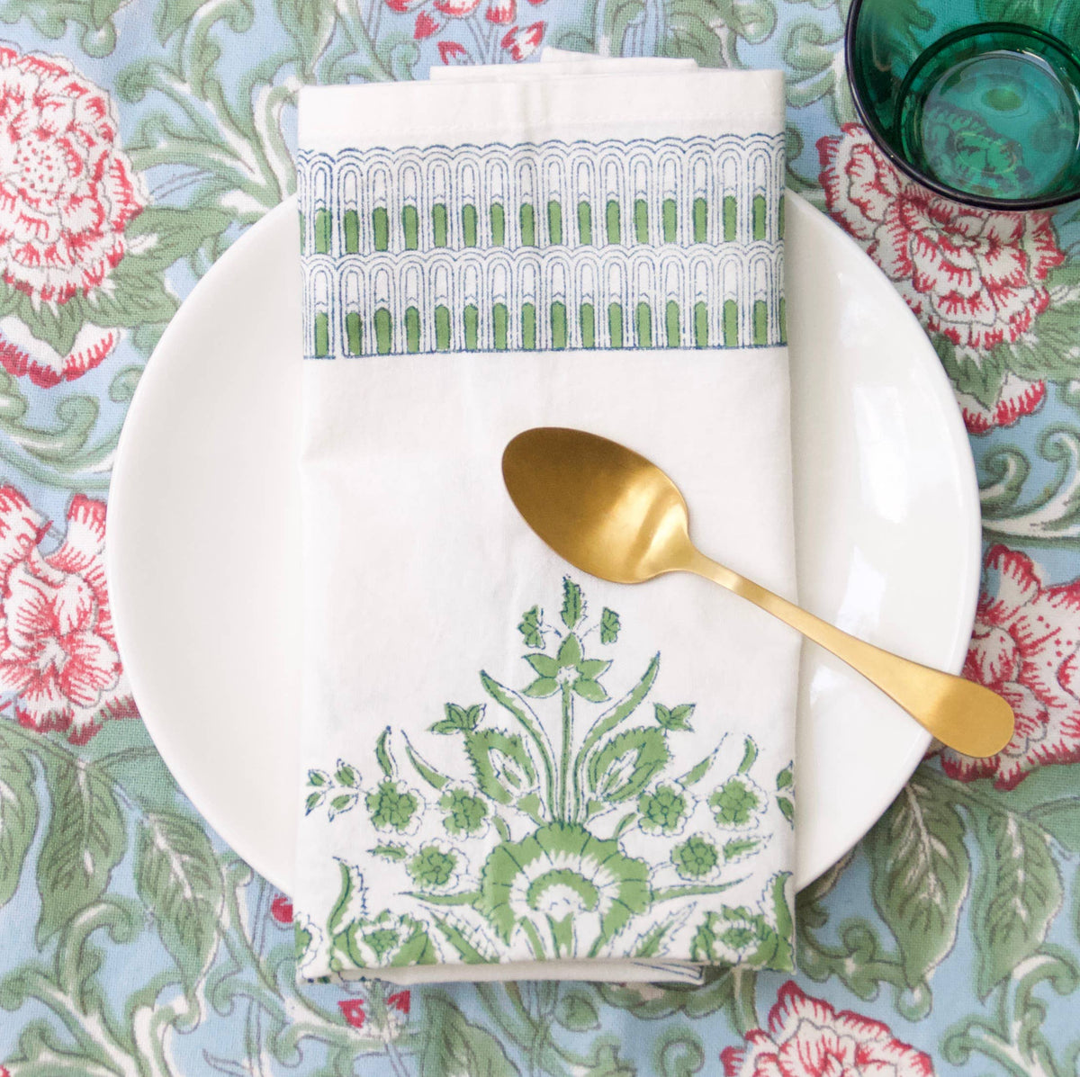 Decorative table setting with a block print patterned napkin, plate, and spoon on a floral tablecloth.