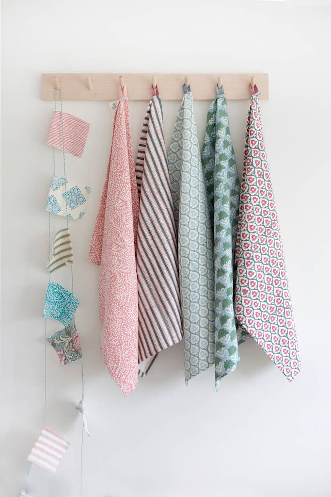 Set of colorful block print patterned dish towels or tea towel hanging on a wooden rack against a white wall.