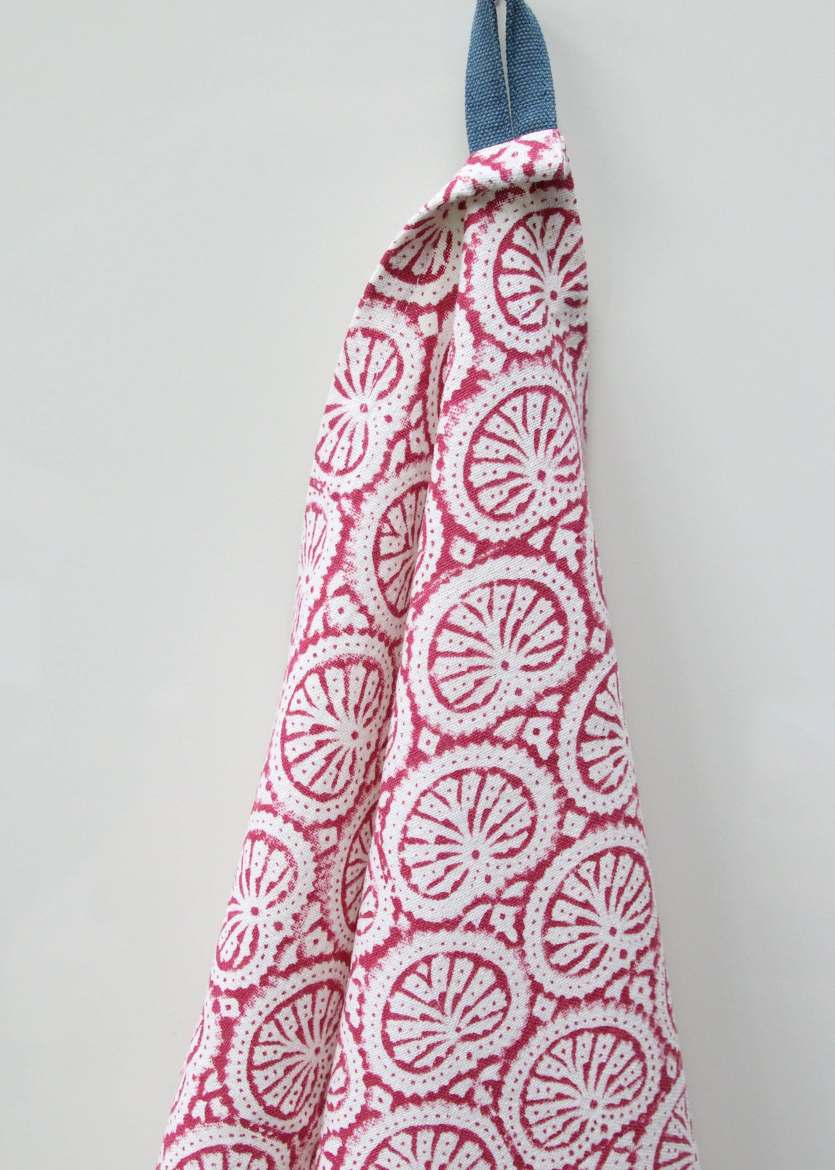Pink and white block print patterned dish towel or tea towel with blue strap on a light gray background