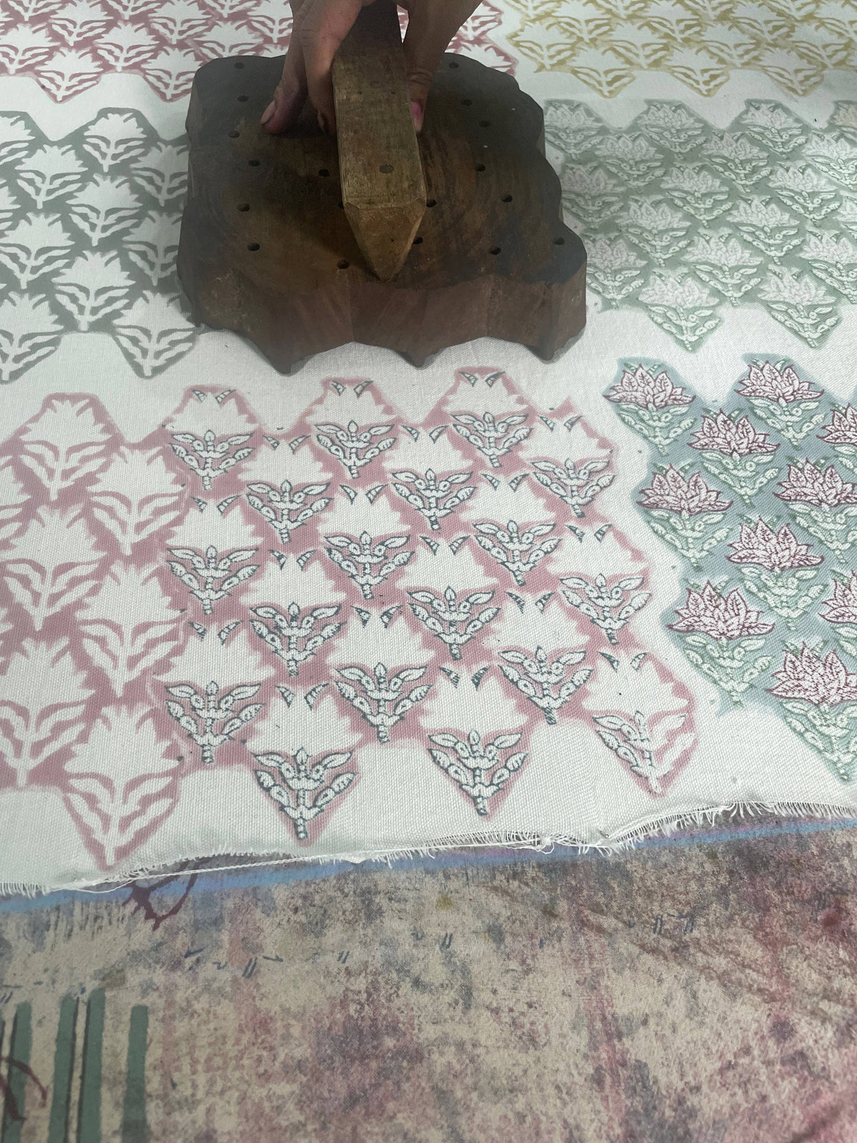 Hand using a wooden block to print a pattern on fabric with a geometric design.