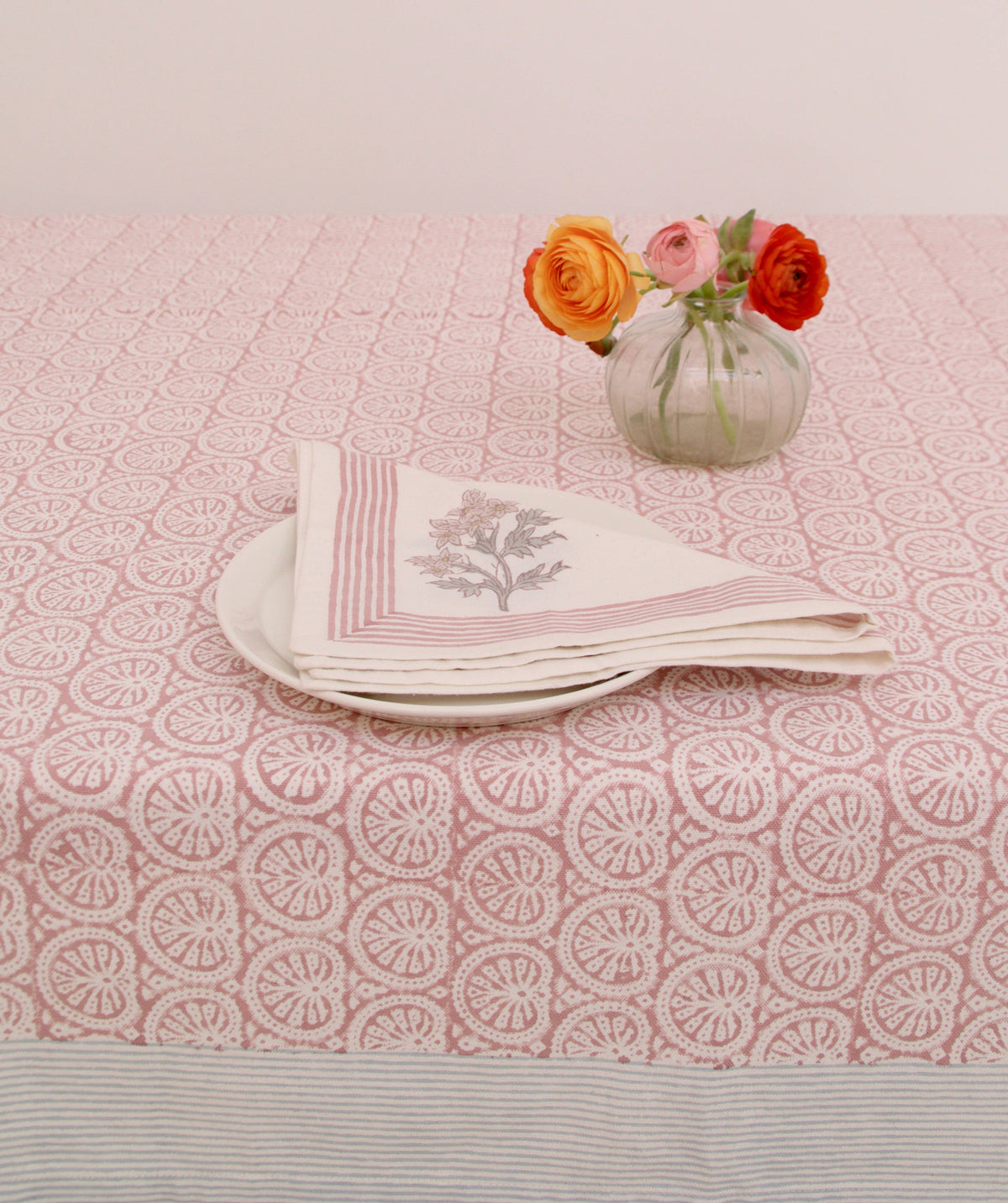 Stack of folded napkins on a pink patterned tablecloth with a small vase of flowers.