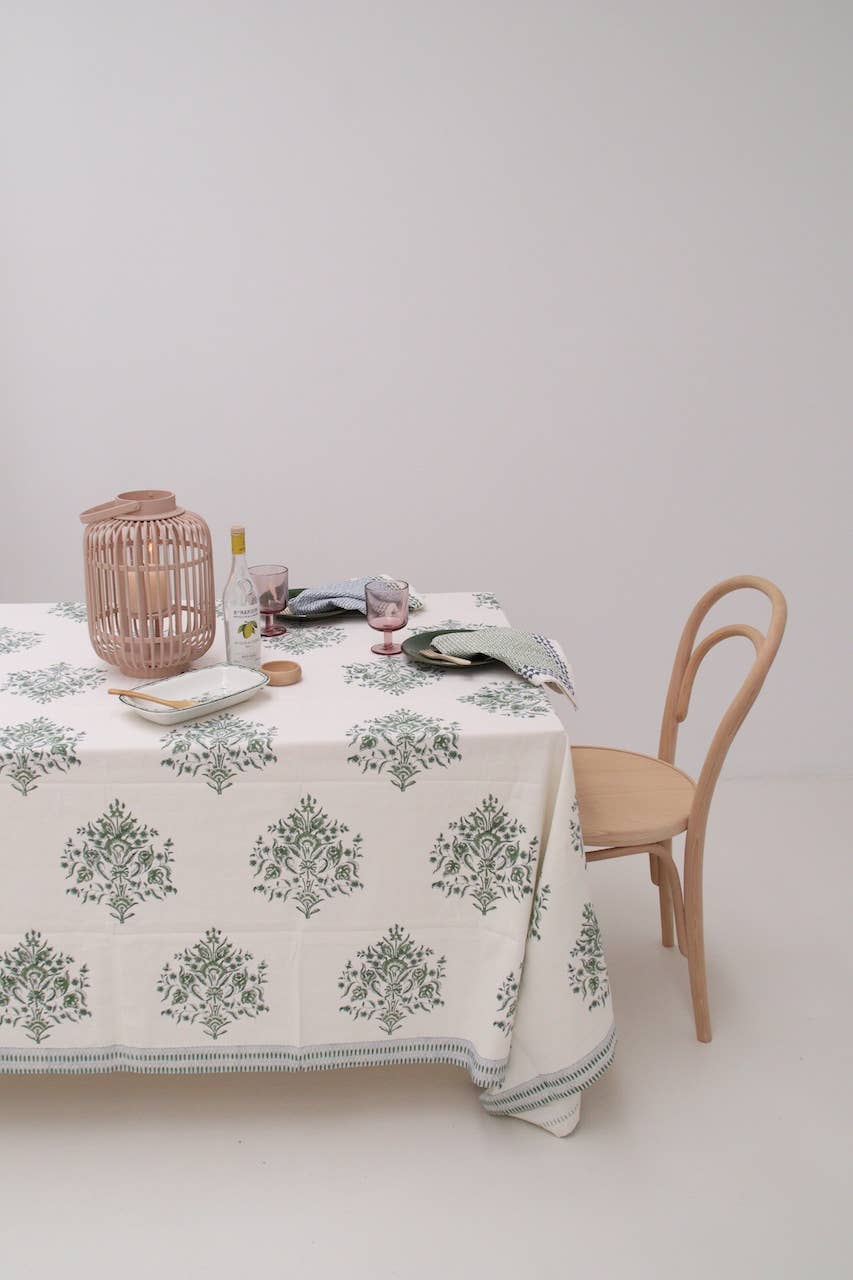 Table with a green, white & blue floral block print tablecloth, wooden chair, and decorative items on a plain background