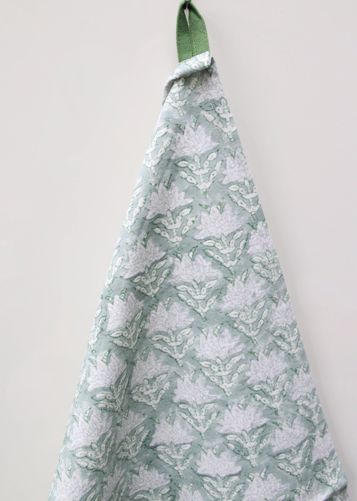 A block print tea towel or dish towel with a floral pattern hanging on a green hook against a white background