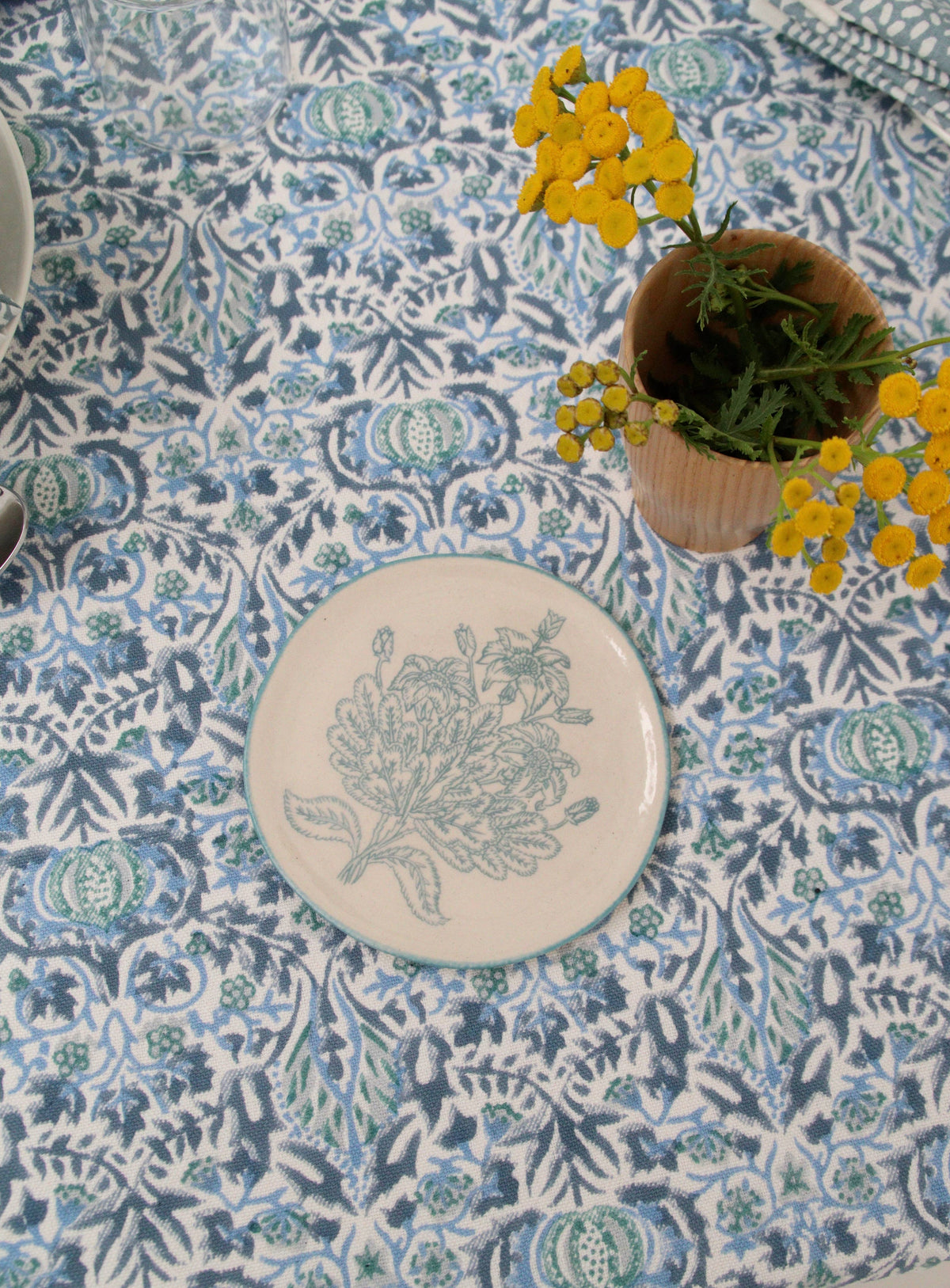 Decorative plate with blue floral design on a patterned tablecloth with yellow flowers.