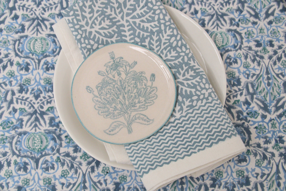 Table setting with a decorative plate, napkin, and cutlery on a patterned tablecloth.