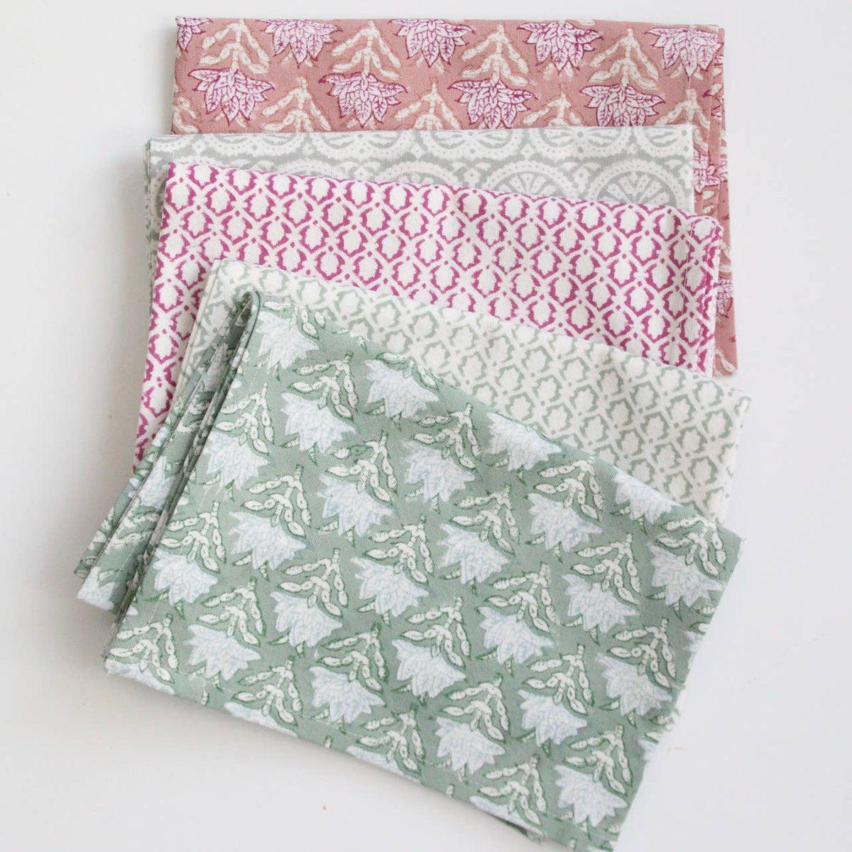 Stack of colorful block print patterned tea towels or dish towels in pink, white, and green on a light background