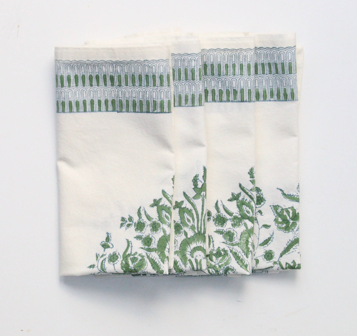White cotton napkins with green floral block print pattern and decorative border on a white background