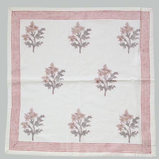 White cotton napkin with pink and green floral block print patterns and a pink striped border on a gray background