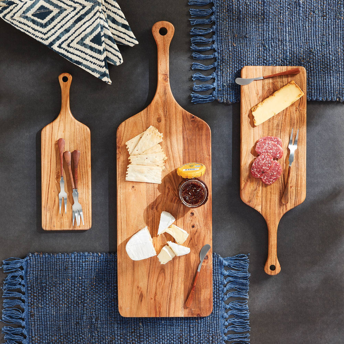 Three wooden cutting boards with various food items on a dark surface with blue textured mats.