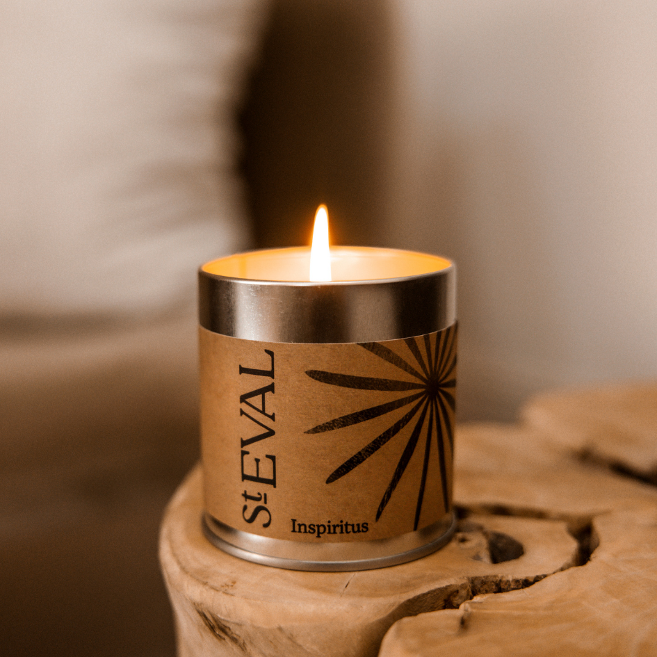 Candle in a St Eval Inspiritus scented candle in a tin container on a wooden surface with a blurred background
