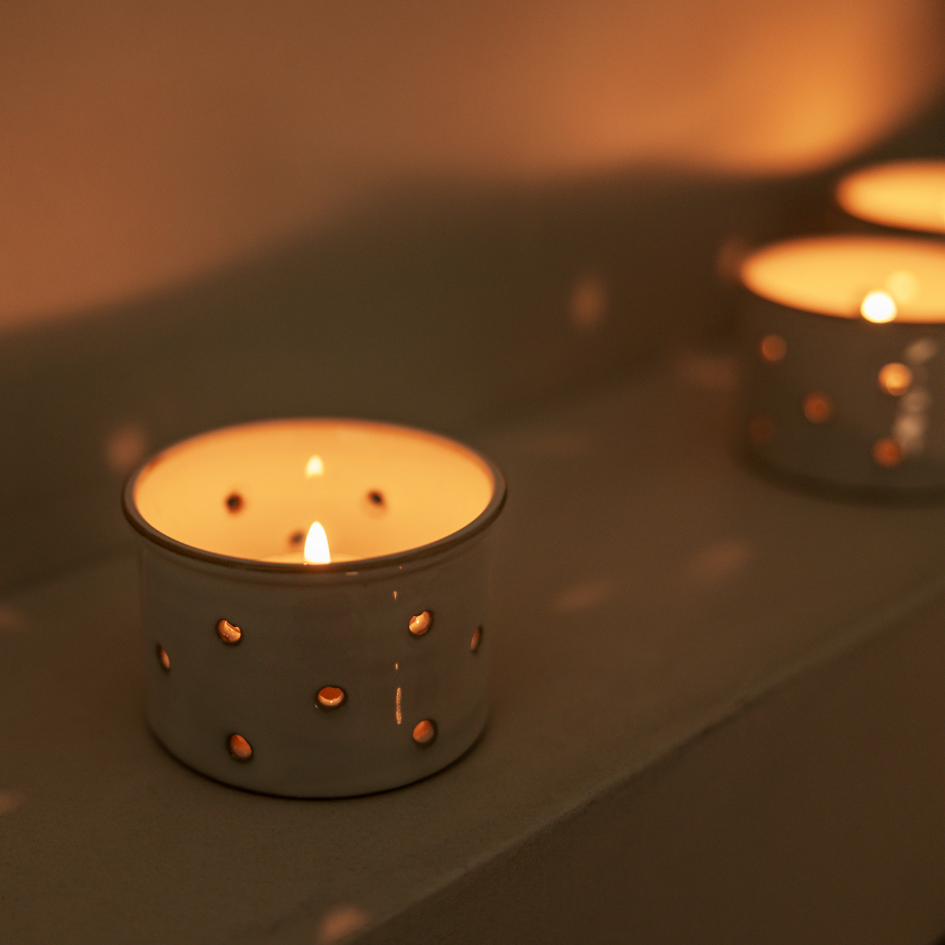 Two lit St Eval scented tea light candles in small ceramic holders on a reflective surface with a blurred background