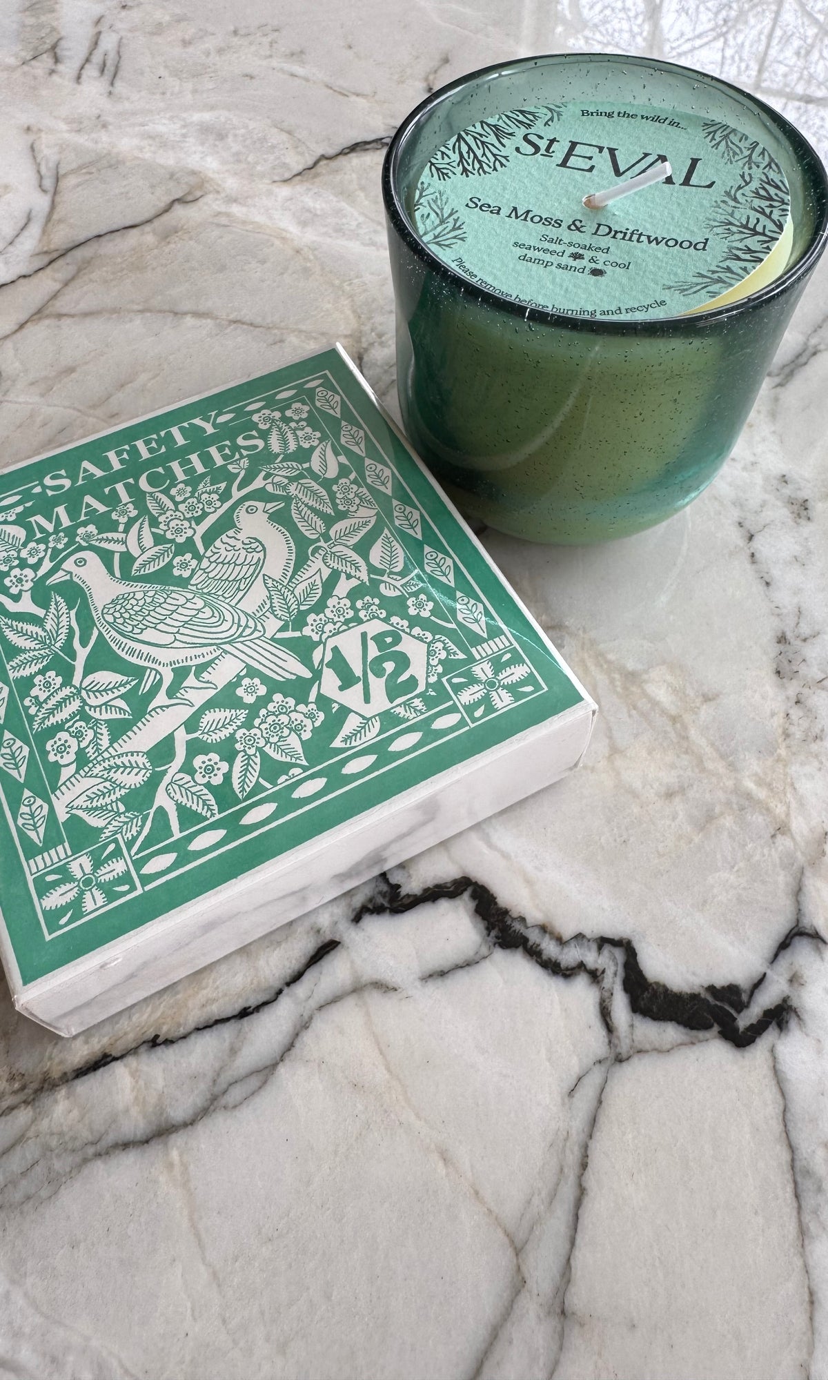 Green St Eval Sea Moss & Driftwood candle and green Archivist Birdy Stamp matches on a marble surface 