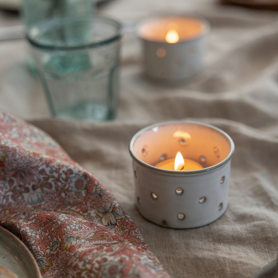 St Eval Candle in a decorative holder on a tablecloth with a glass and another candle in the background.