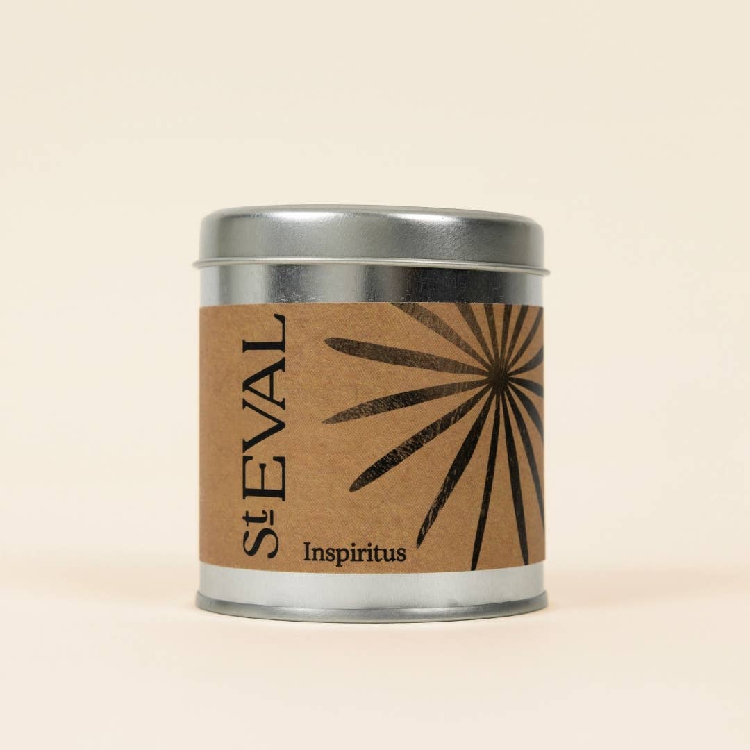 A St Eval Inspritus scented tin candle with a silver lid and a brown kraft paper label featuring a black sunburst design and the text 'st EVAL Inspiritus'.