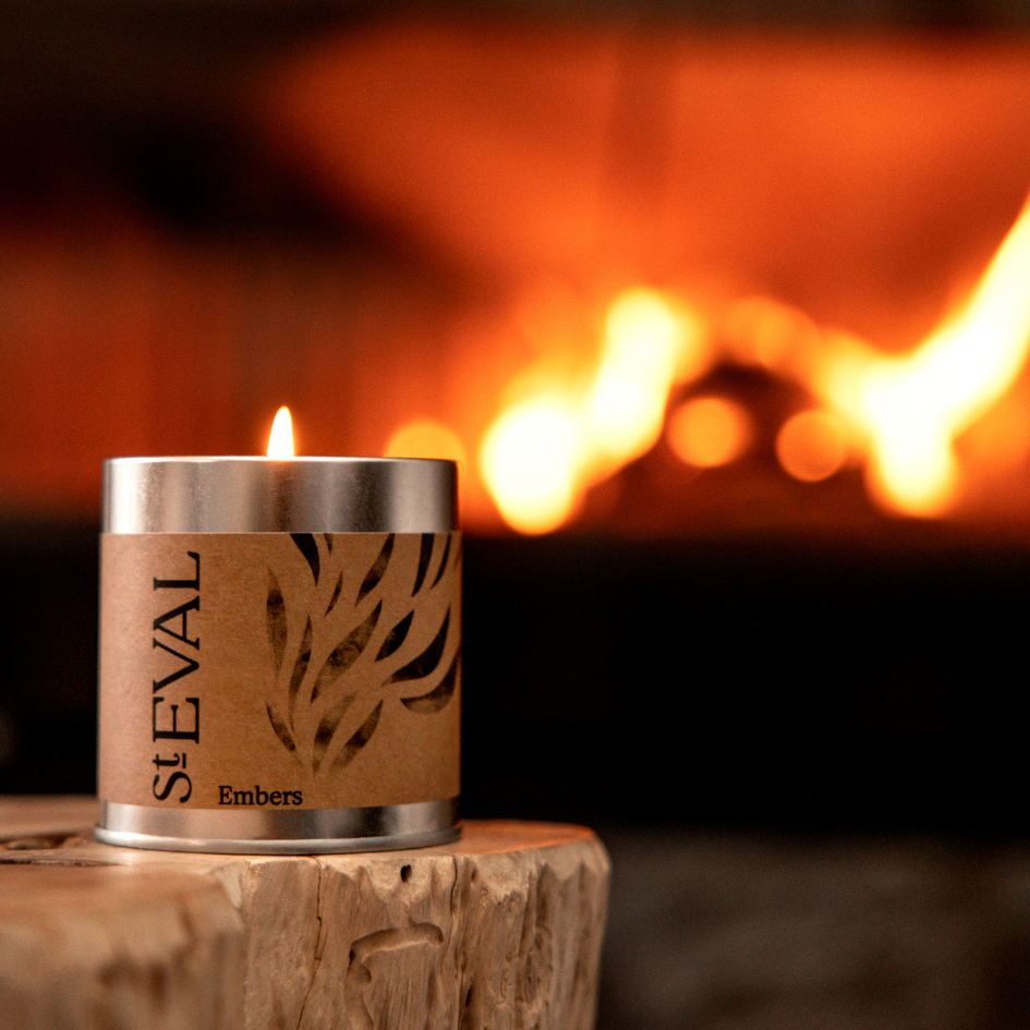 Scented tin Candle labeled 'St. Eval Embers' in front of a fireplace