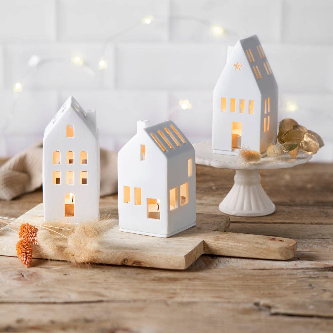 Three white house-shaped candle holders on a wooden surface with a soft, blurred background.